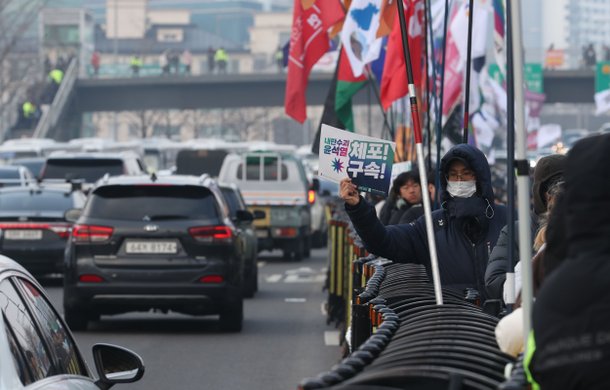 2024년 1월 6일 오후 서울 용산구 한남동 대통령 관저 근처 도로에서 진보시민단체주최로 열린 윤석열 즉각체포 긴급행동 집회에서 한 참가자가 지나가는 차량에 피켓을 들어보이고 있다. /전기병 기자